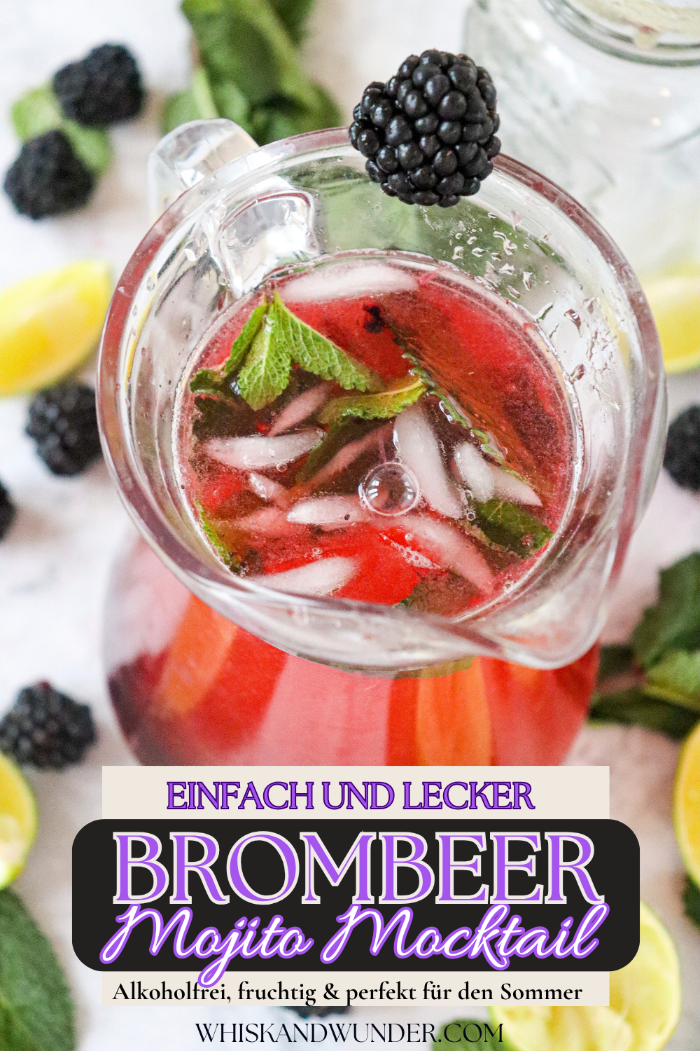 Ein erfrischender Brombeer-Mojito-Mocktail in einer Glaskaraffe mit Eis und Minzblättern, umgeben von frischen Limettenscheiben und Brombeeren.