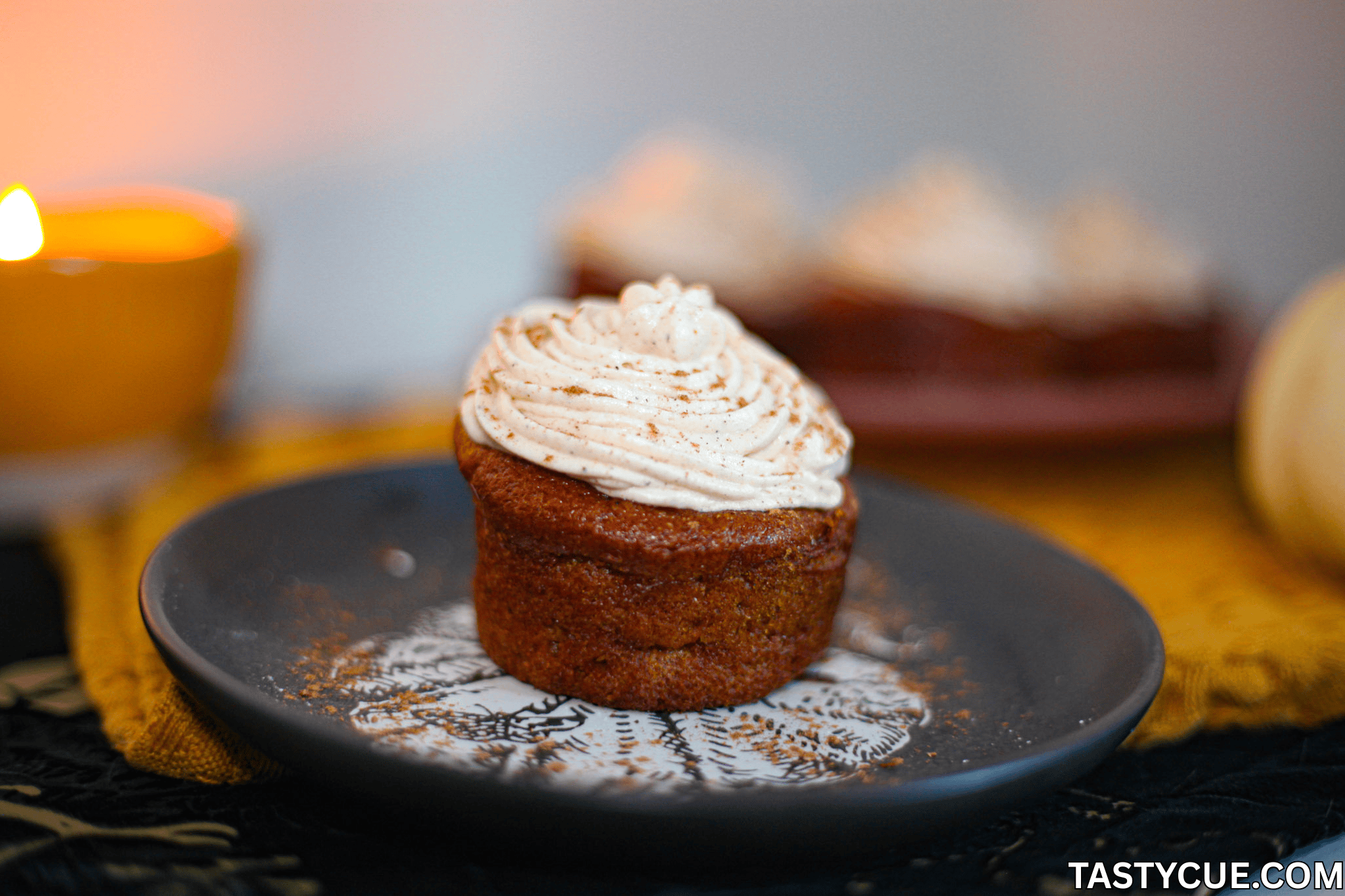 Kürbis-Cupcake mit Chai-Frischkäse-Frosting auf einem dekorativen Teller, umgeben von herbstlicher Atmosphäre.