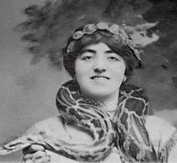 Svartvit porträttbild av Stuertz hustru, Dagmar Franciska Hansen, vid Barnum & Bailey Circus, 1913. En mörkhårig kvinna, med håret uppsatt enligt 1910-talets mode, med mörka ögon, bär en stor boaorm runt halsen. Hon ler mot kameran.