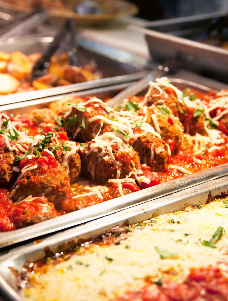 Haitian-style meatballs in tomato sauce with grated cheese and macaroni au gratin in a buffet tray