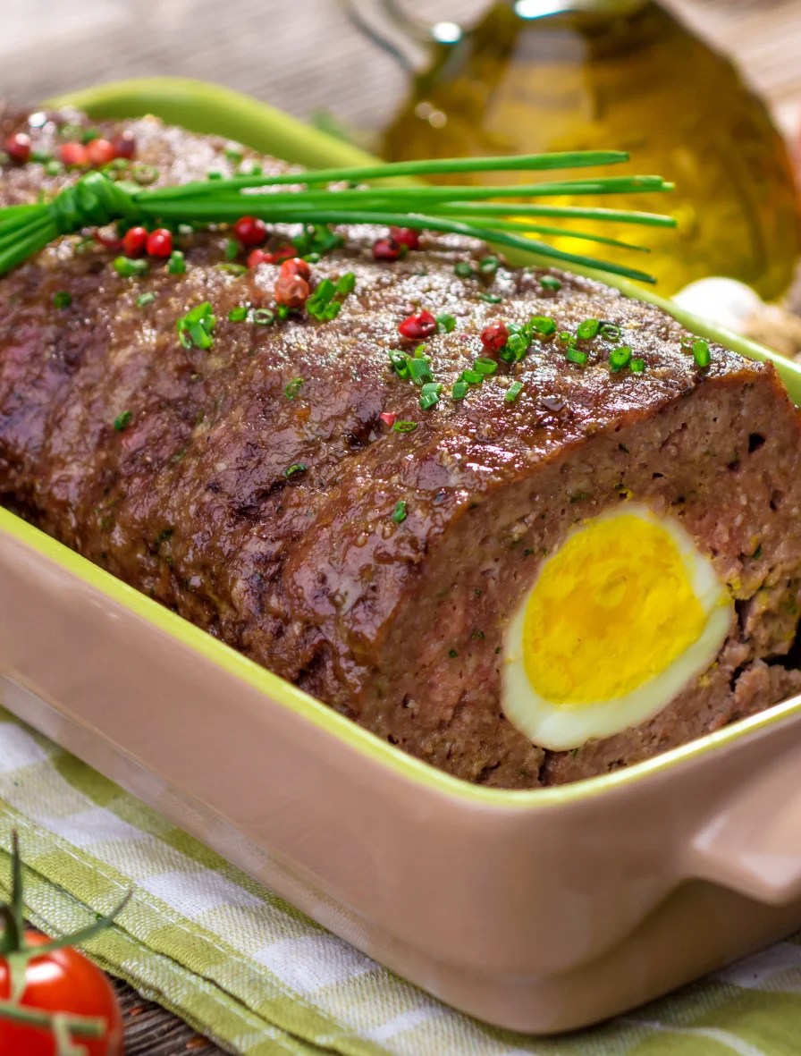 Haitian-style meatloaf with boiled egg center, garnished with herbs and peppercorns