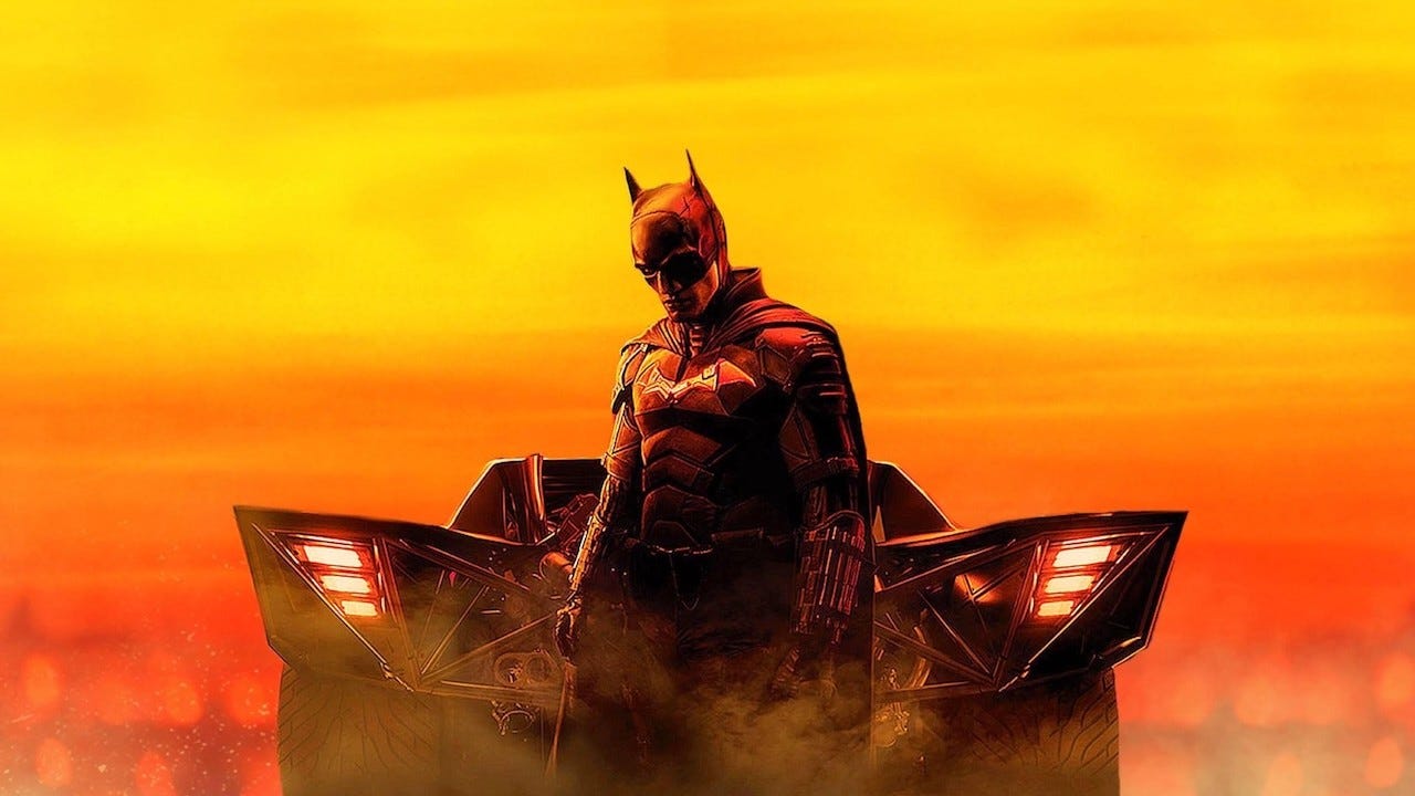 Batman stands in front of the muscle-car Batmobile in key art for The Batman