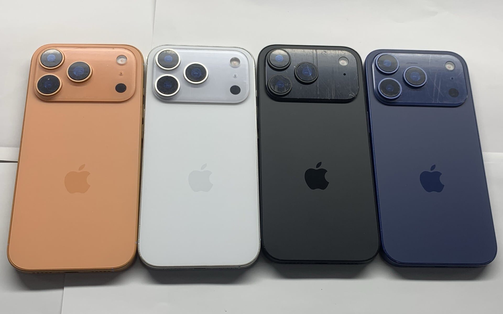 Four iPhone Pro models with frosted glass backs lined up on a white surface