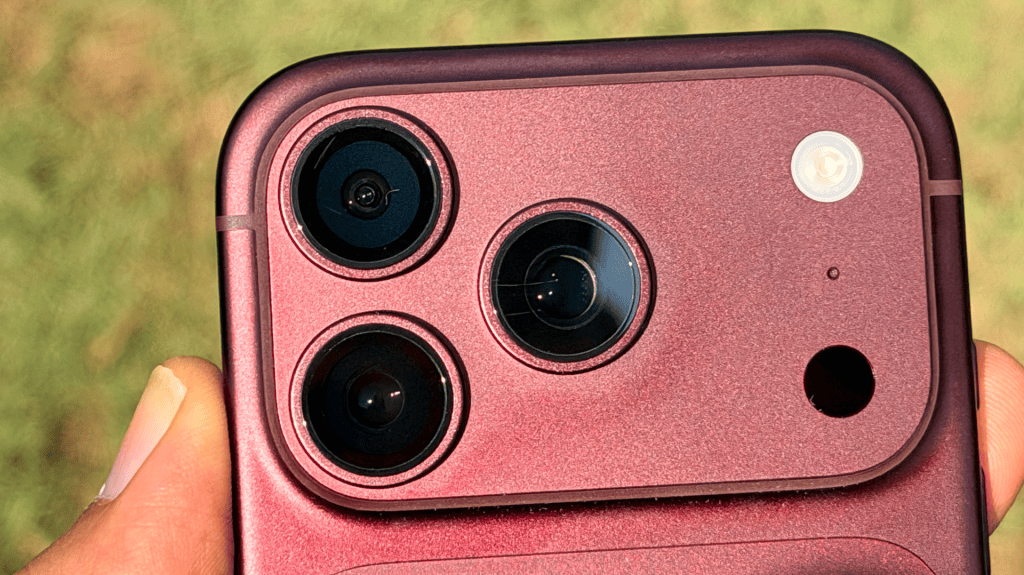 Close-up image of the back of a smartphone showcasing three camera lenses and a flash, held in a hand against a blurred green background.