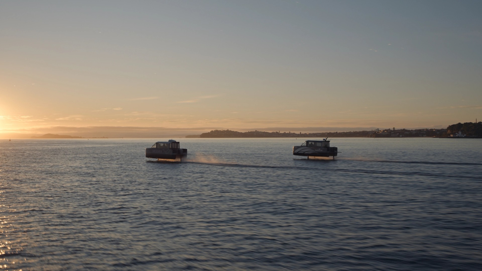Two Vessev VS-9 electric ferries hydrofoiling above calm water at dusk