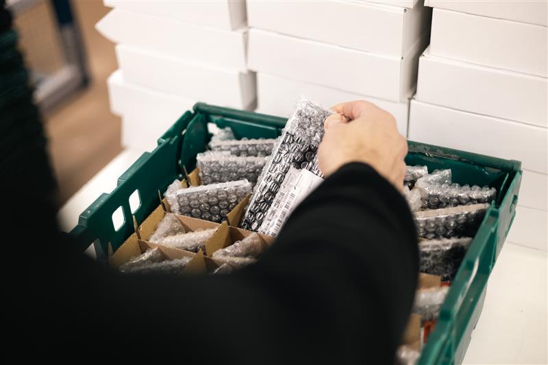 Warehouse operative handling bubble-wrapped IT assets in a divided green storage crate as part of an ITAD processing and fulfilment operation.