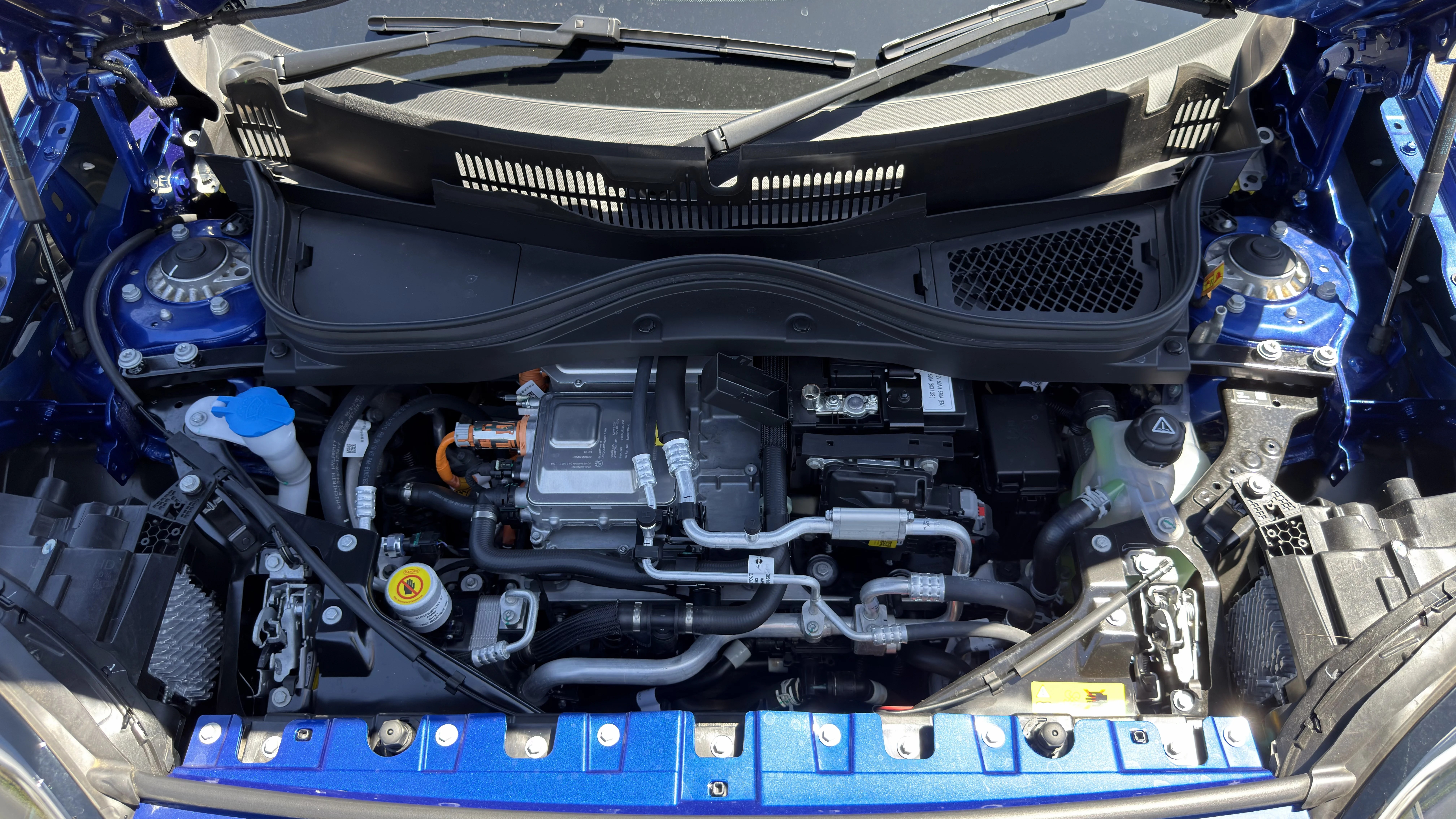 2026 Mini Aceman JCW front powertrain with electric motor module, orange high-voltage cables, coolant and washer reservoirs.