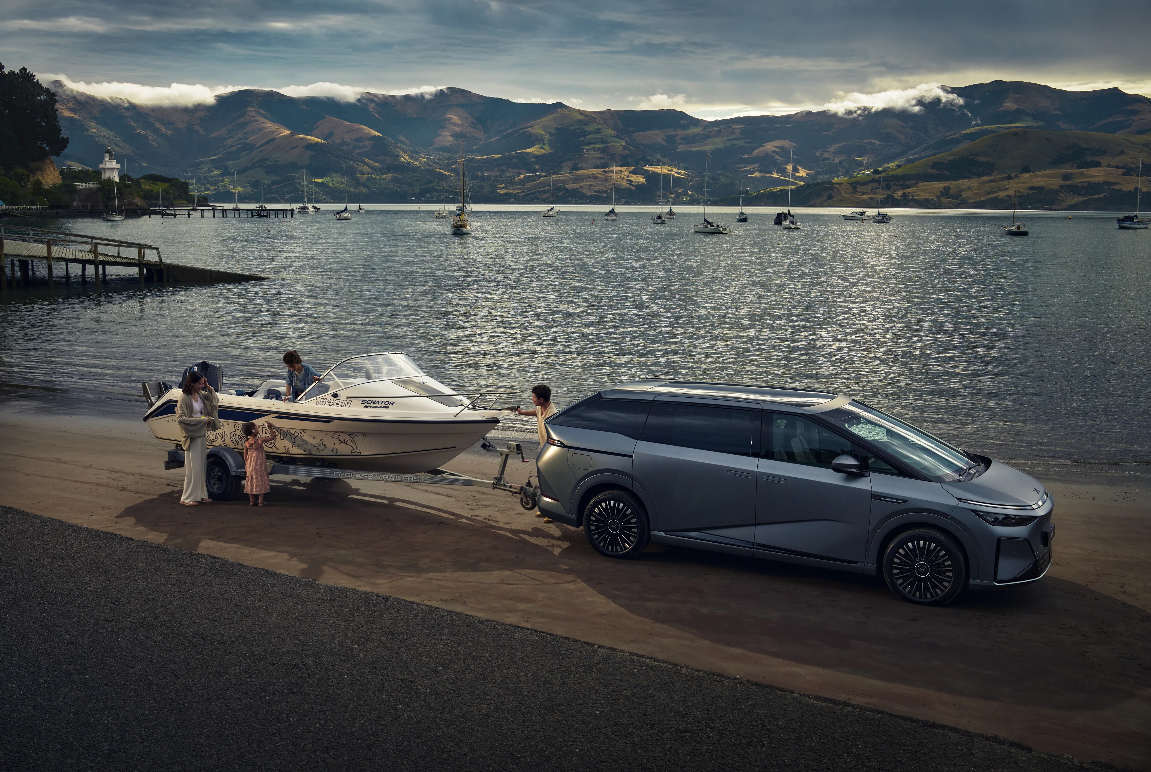 Electric minivan towing a boat on a beach with boats in the bay