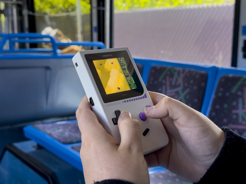 Someone playing ModRetro Chromatic Gameboy handheld in cloud color on bus