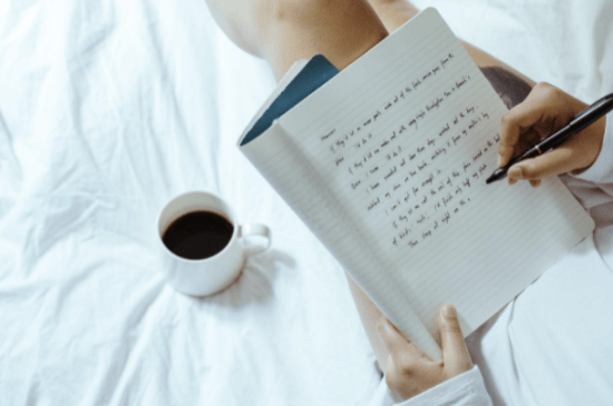 compelling biographies, a woman writing in a notebook next to a cup of coffee