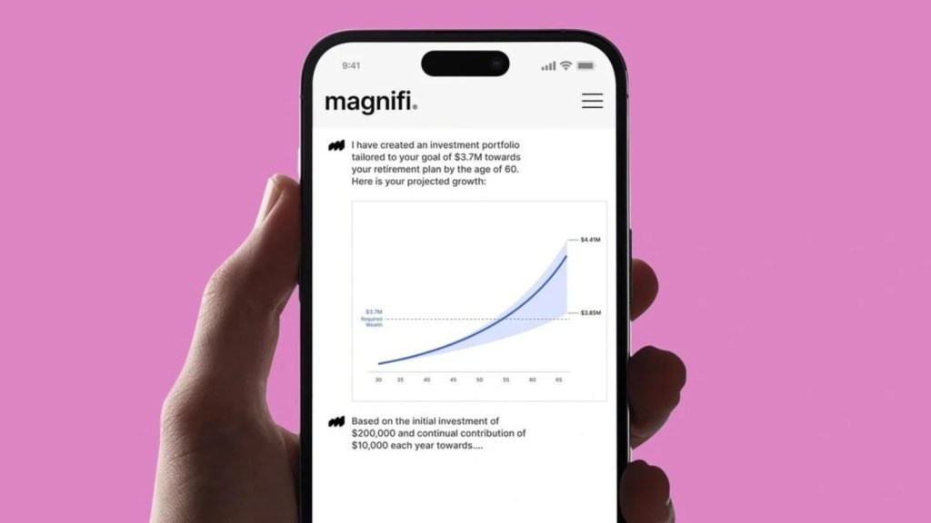 A friendly, cartoonish robot stands on a desk next to a large curved monitor displaying financial market charts. A hand holds a smartphone showing a "magnifi." app screen with an AI-generated investment portfolio and a projected growth graph.