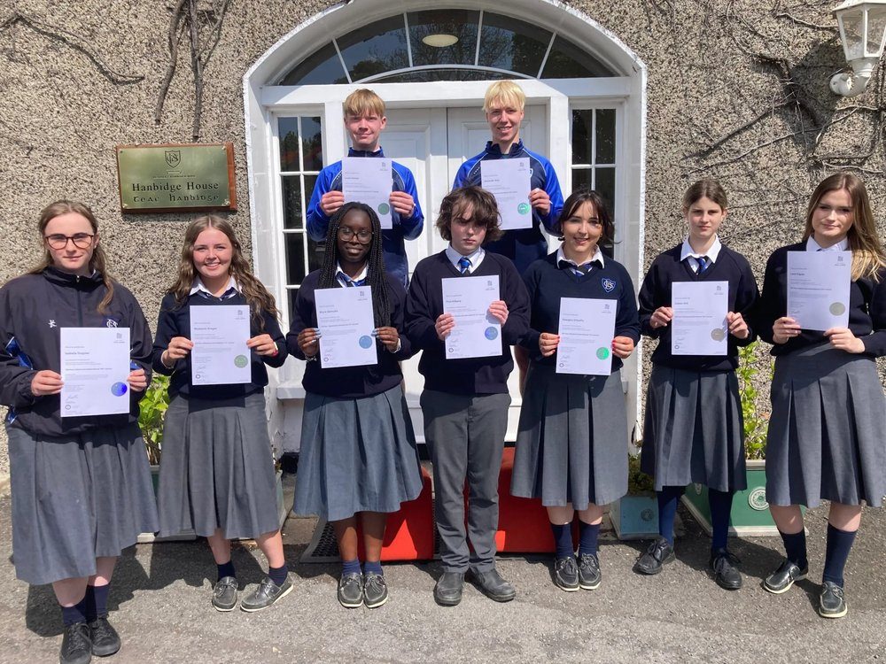 A mixed Transition Year class holding TEFL certificates outside the front door of their school