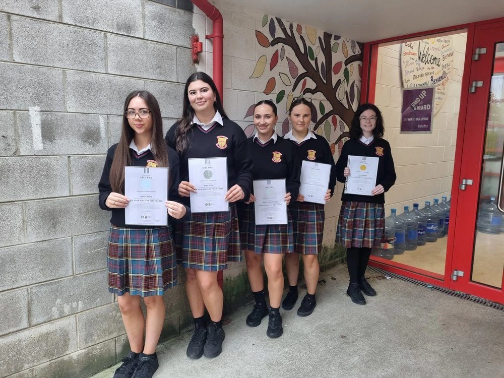 Five Transition Year students holding their TEFL certificates at the entrance to their school