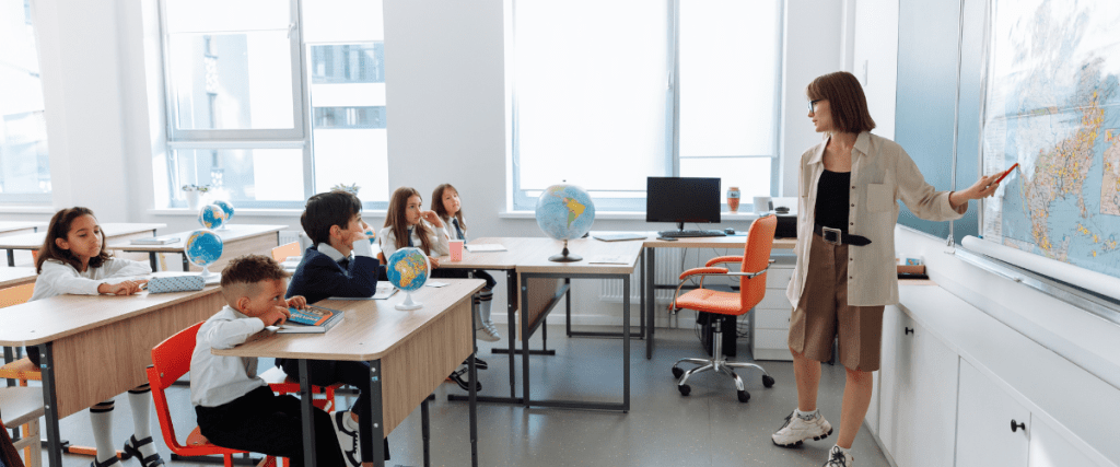 teacher with a room full of school kids pointing at a world map