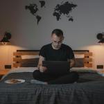 a man using a laptop while sitting on a bed