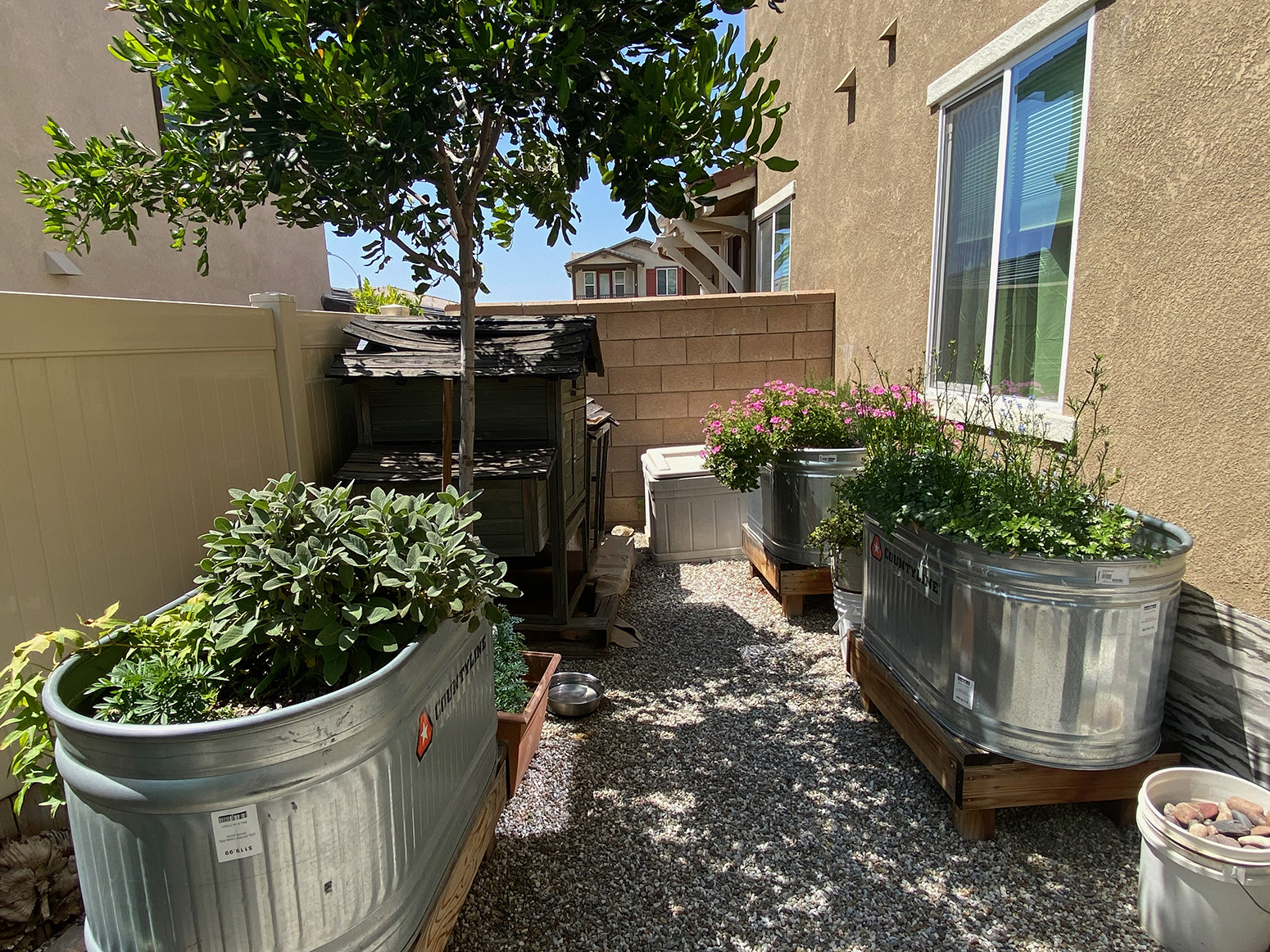 Shot of side yard with jellybean rocks, brick walling, and metal planters.