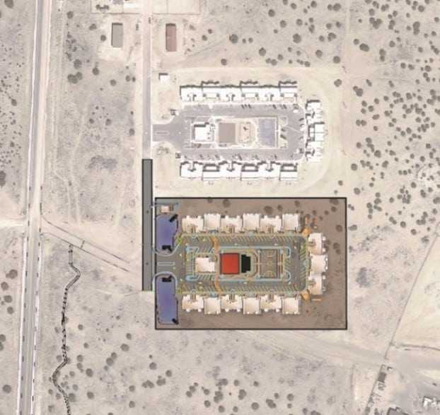 Aerial view of a planned residential development surrounded by arid land, showing outlined plots and roads with a nearby existing neighborhood.