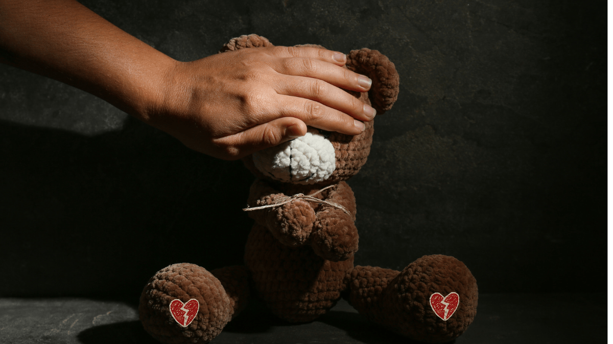 A small brown teddy bear whose hands are tied in front and whose eyes are covered by an adult's hand. This represents the trauma of childhood labels and explores a theme of the psychological thriller Cobra Orchard by author Terveen Gill.
