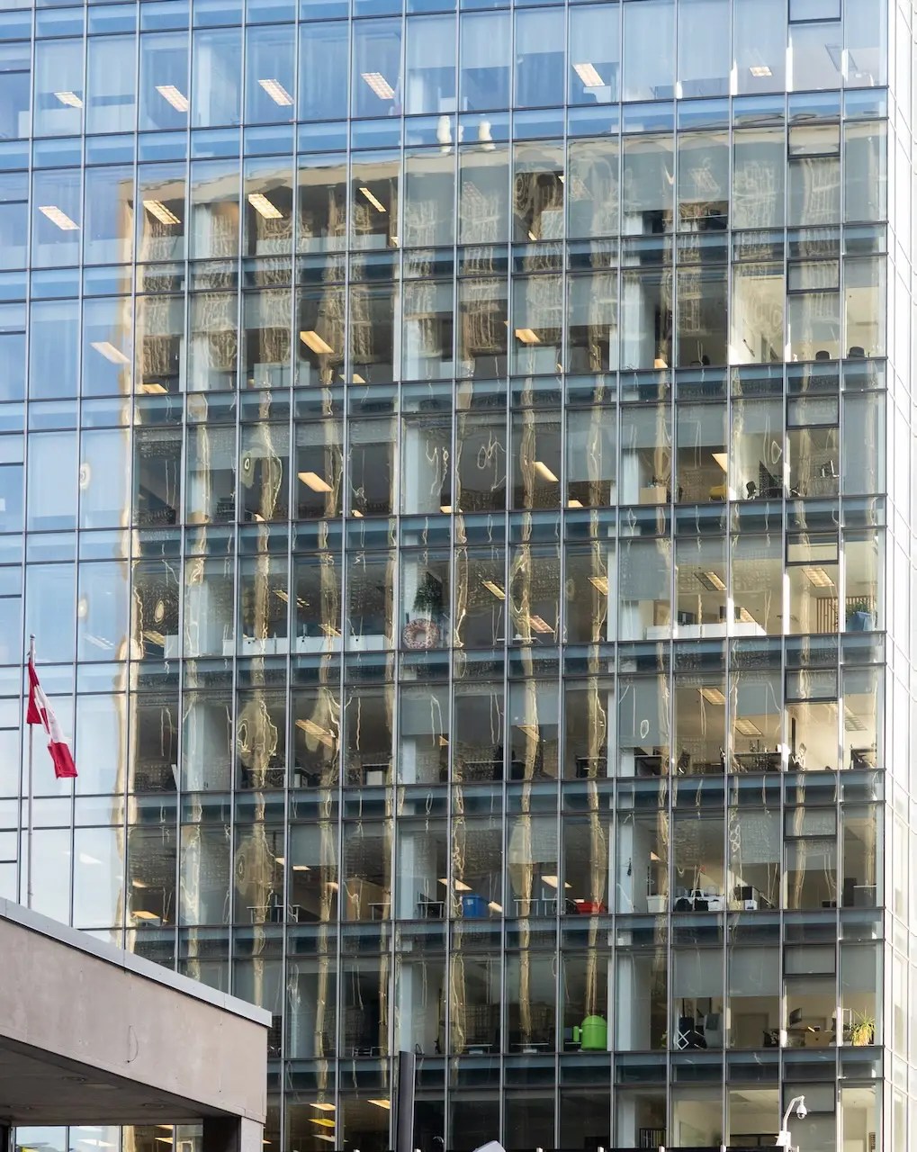 A building reflected in the windows of another building. A Canadian flag is in frame.