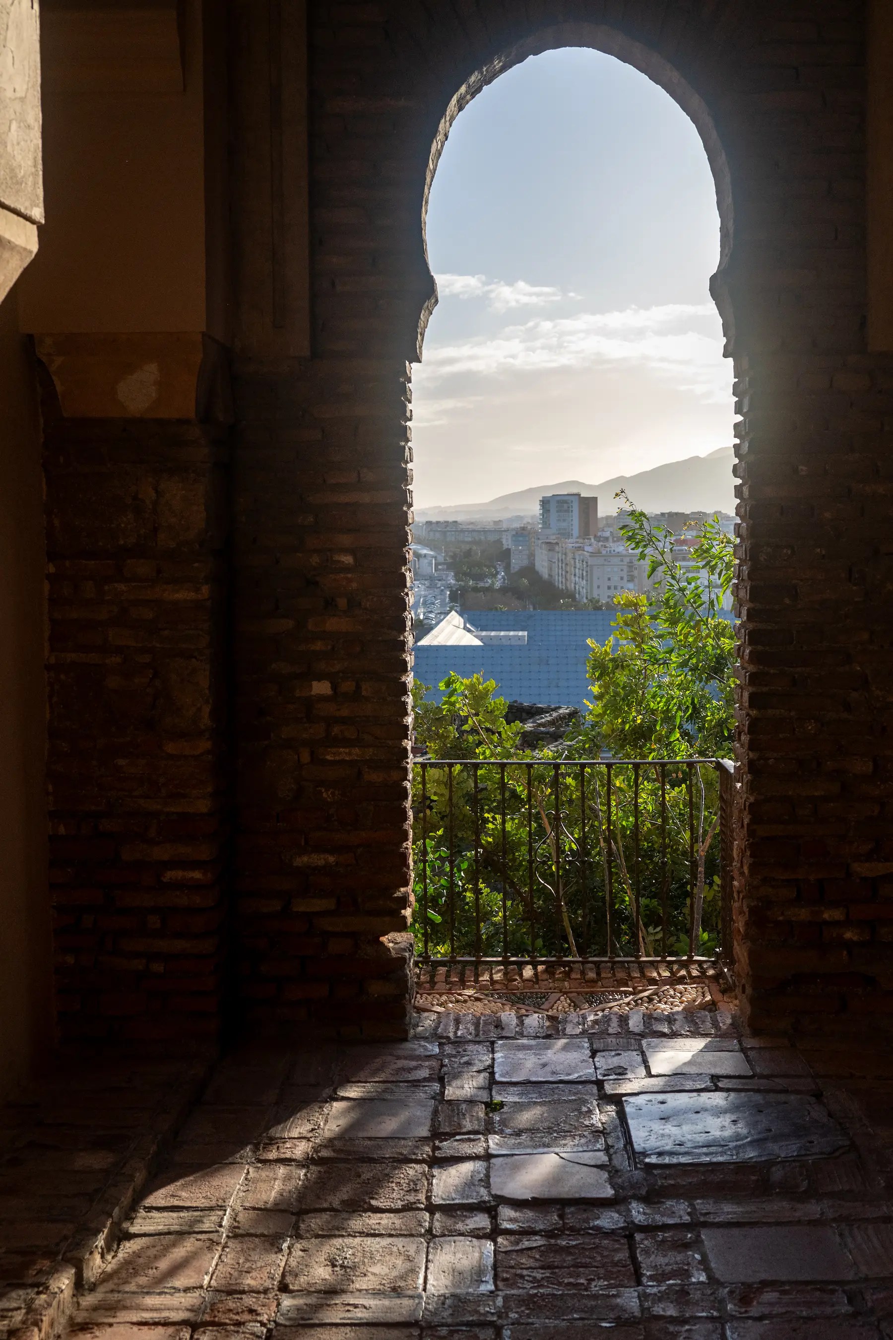 View of a city and distant mountains through a tall, arched brick doorway.