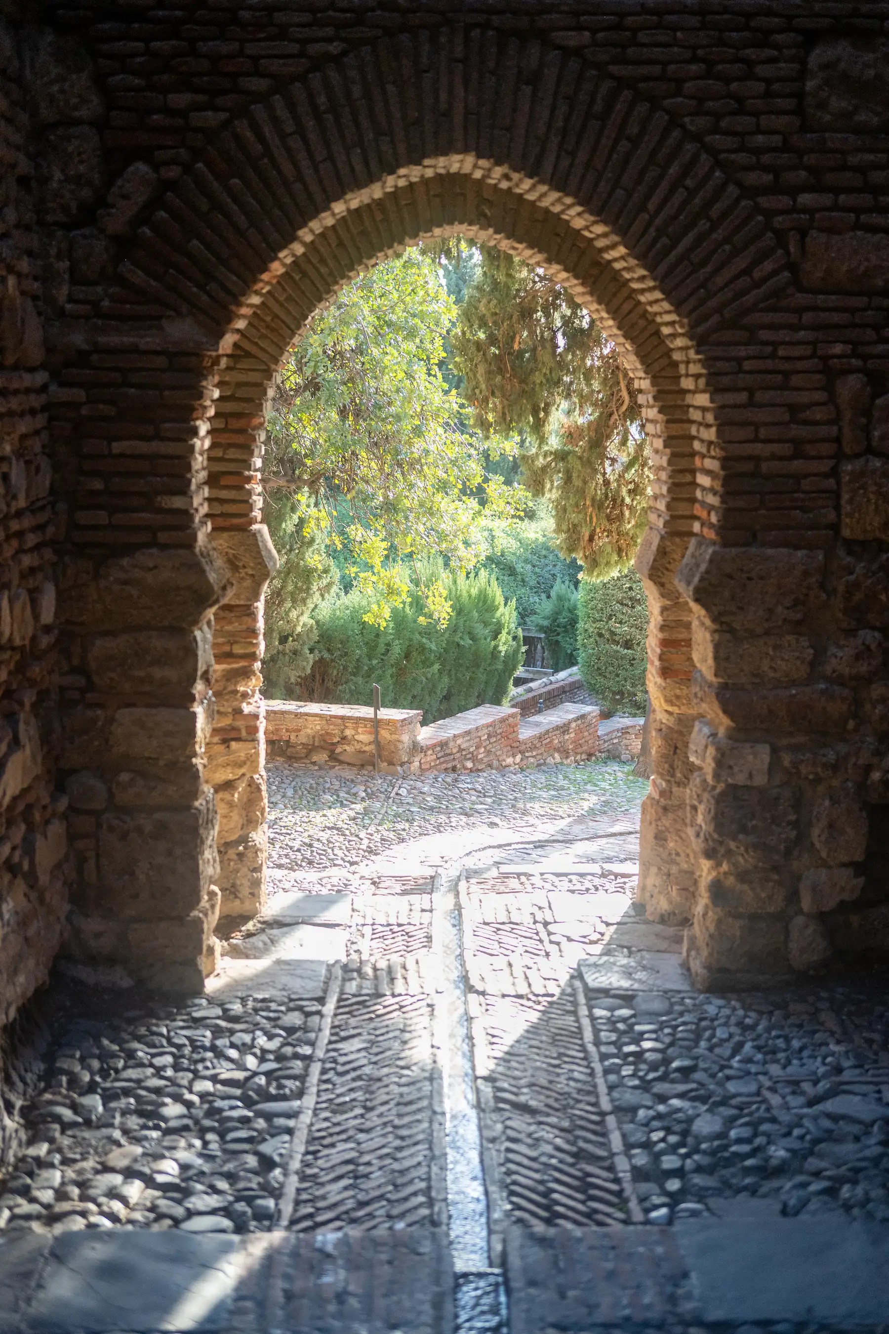 A stone and brick archway framing a view of a cobblestone garden path