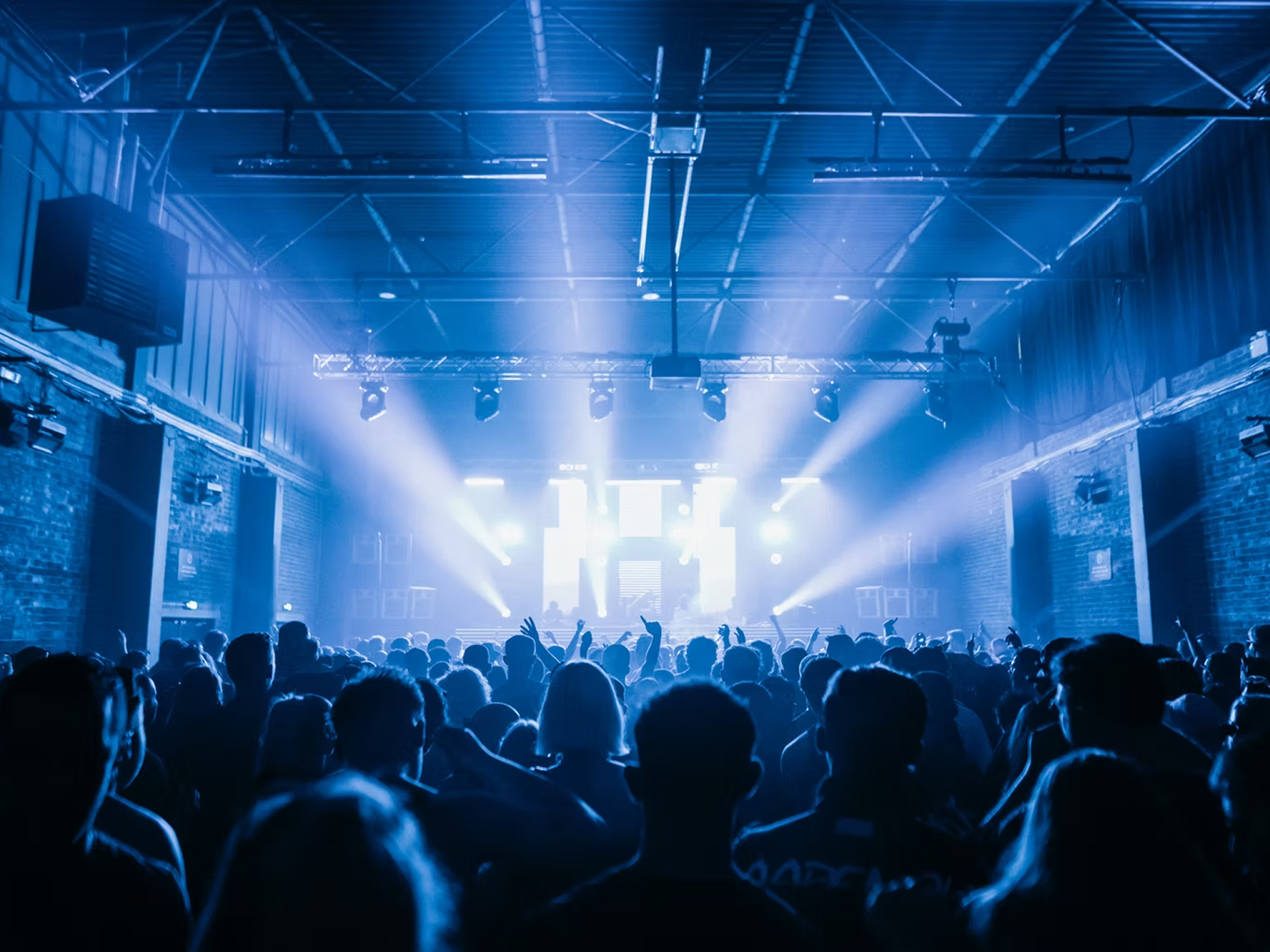 A large audience of people dancing in front of a DJ on stage.