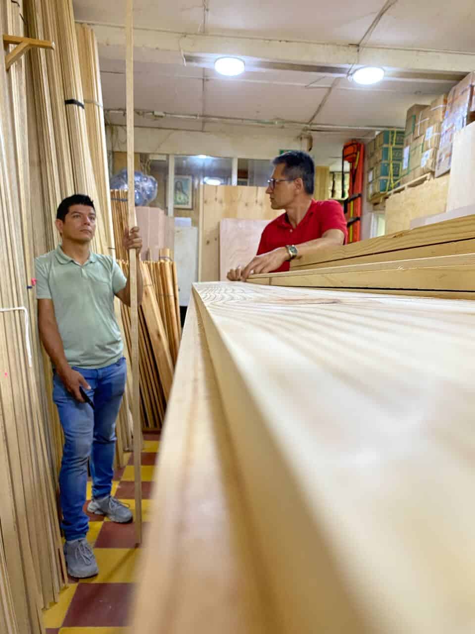 Zwei Männer in Holzhandlung, Fokus auf Holzplatten und -stangen.