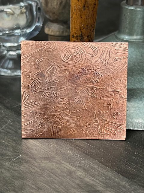 Engraved square metal plate with abstract designs.