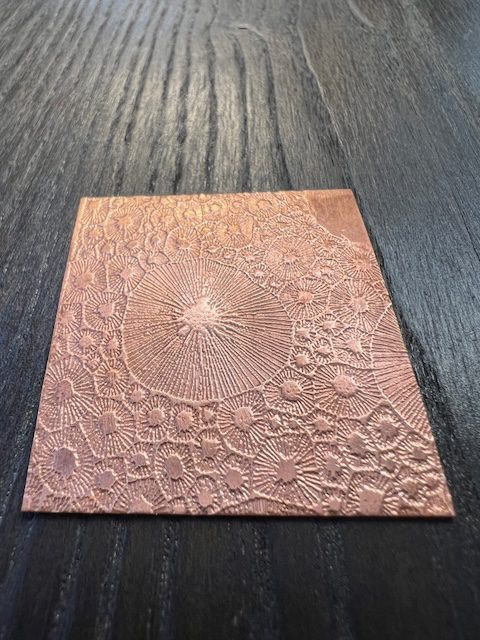 Etched copper plate on dark wooden surface.
