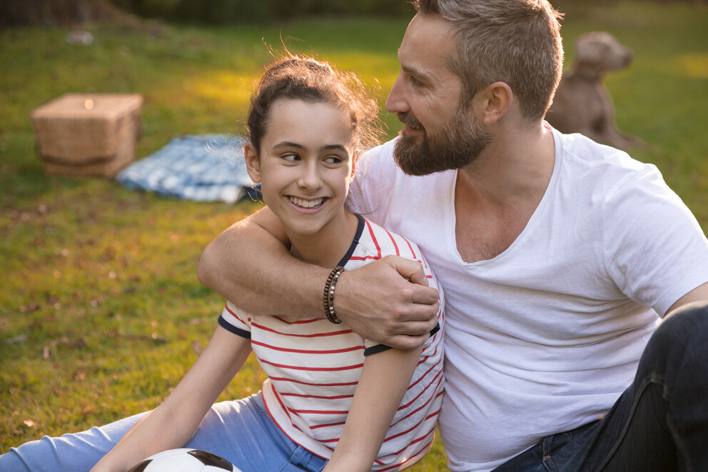 dad hugging teen daughter sitting in grass