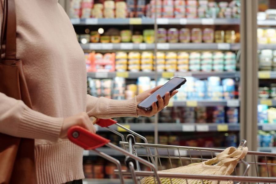 Woman grocery shopping while checking a meal planning list on her phone