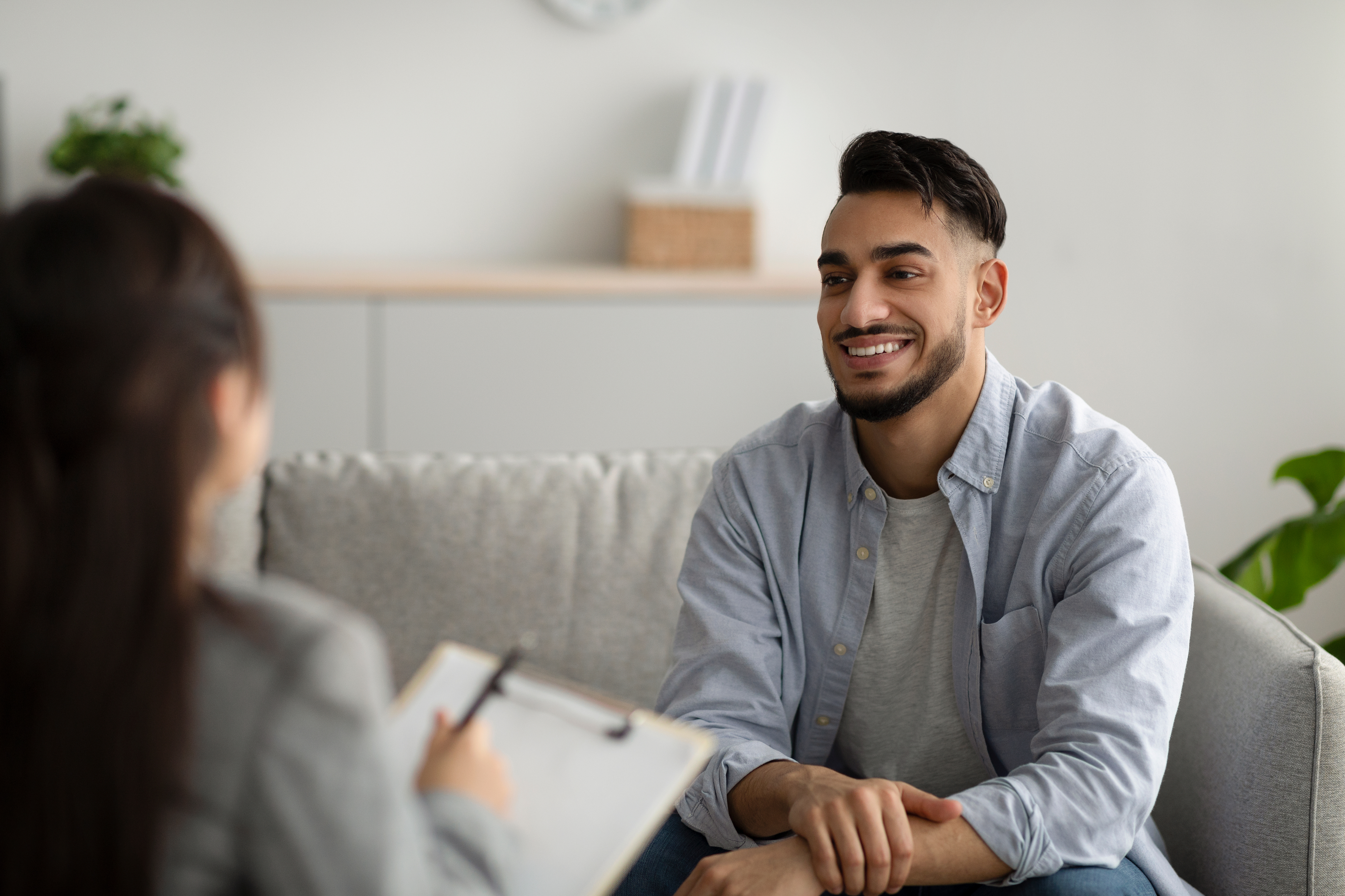 Effective psychotherapy. Happy middle eastern man talking to his psychologist, sharing therapy results with counselor, receiving professional help at mental health clinic