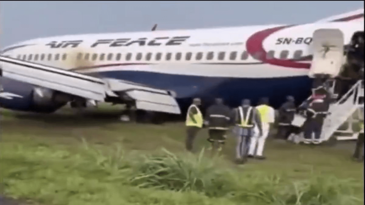 An Air Peace Boeing 737-300 rests on a grassy field after overrunning the runway at Port Harcourt Airport. Passengers are seen deplaning via a mobile stairway as emergency responders assist at the scene.