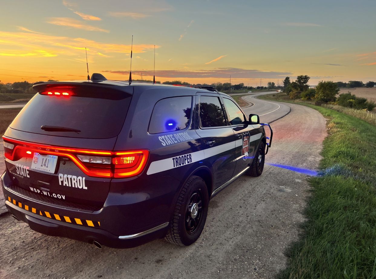 An image of a Wisconsin State Patrol squad car parked on the side of the road with its lights engaged.
