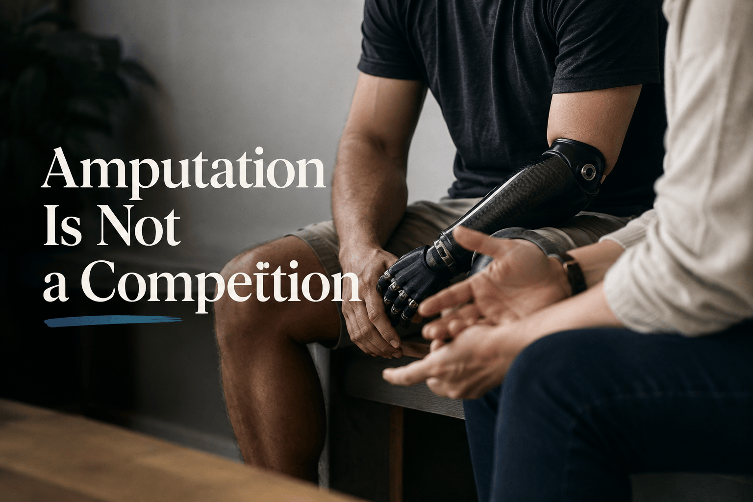 Two people seated in conversation, one wearing an upper-limb prosthesis, with the words “Amputation Is Not a Competition.”