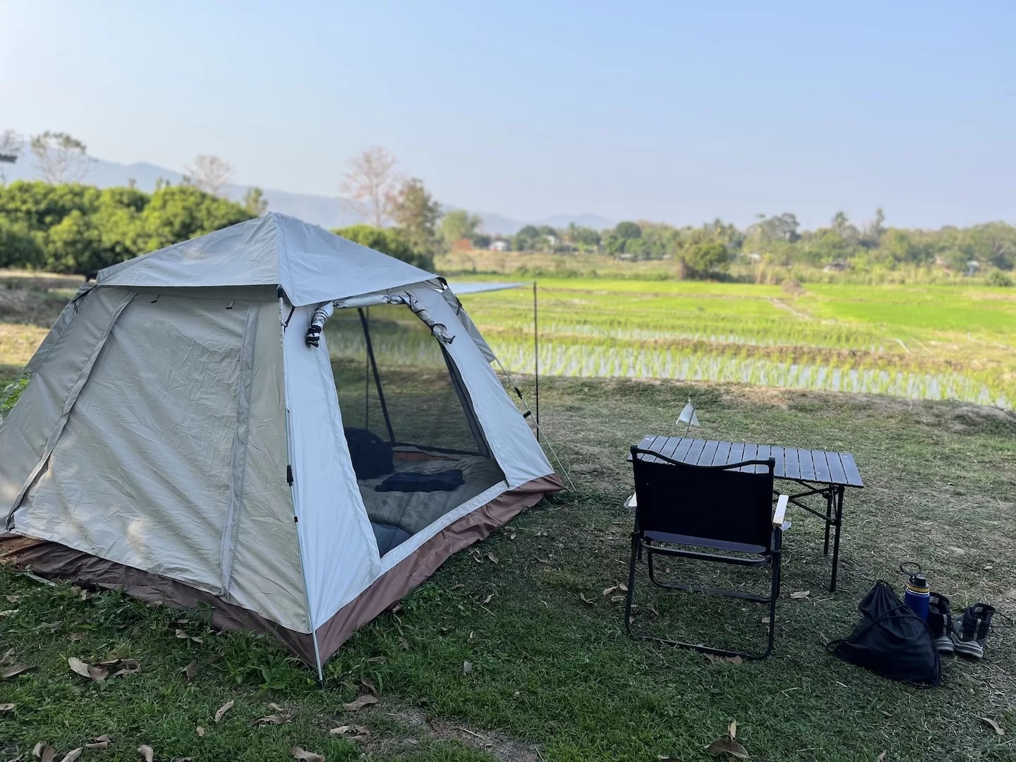 tent pitched on the grass next to green rice fields at the farmer farm stay in chom thong, below doi inthanon