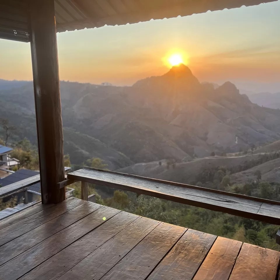sun setting over jagged mountains, seen from the wooden balcony of a bar near ban ja bo on the mae hong son loop