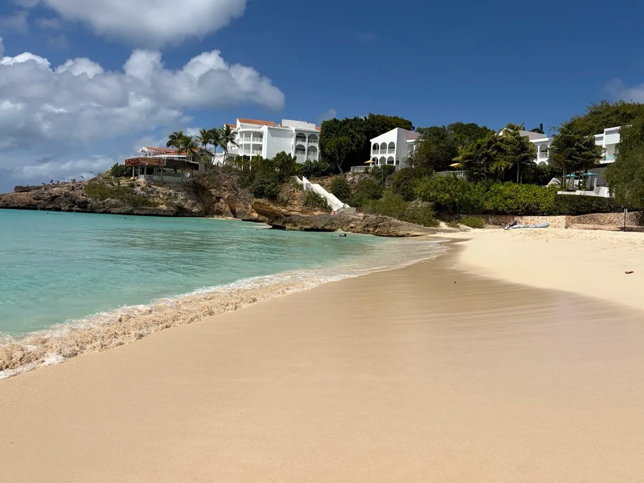 view of the end of meads bay with perfect golden sand and turquoise waters, with the Malliouhana resort rising up on a cliff behind