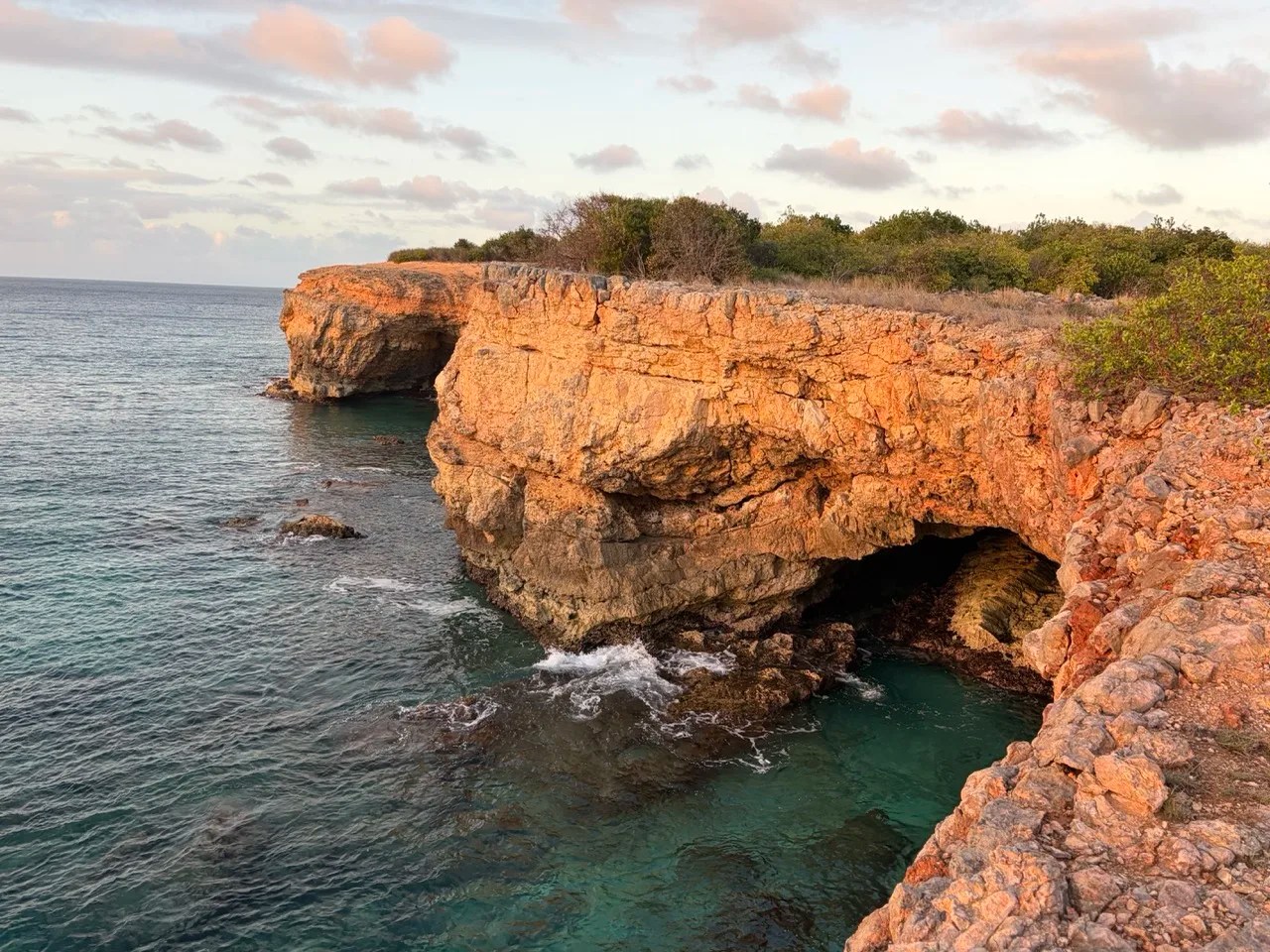 cliffs with caves at the edge of anguilla dropping into the turquoise water, reflecting a glow from the setting sun