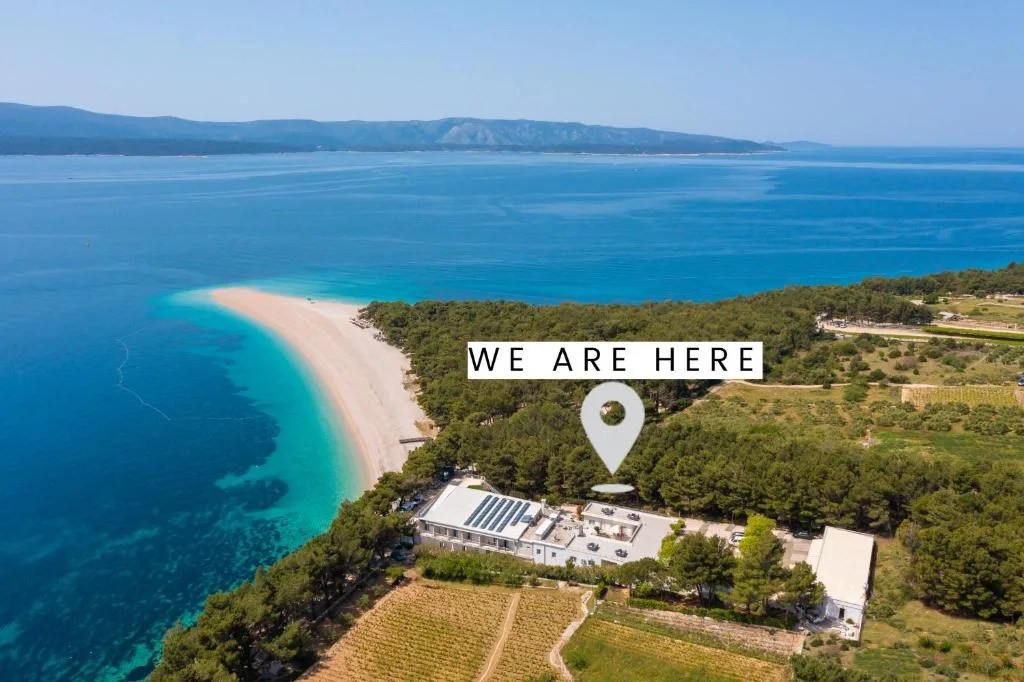 an aerial view of a resort marked by a 'we are here' pin right next to the zlatni rat beach poking out into the sea in bol, croatia