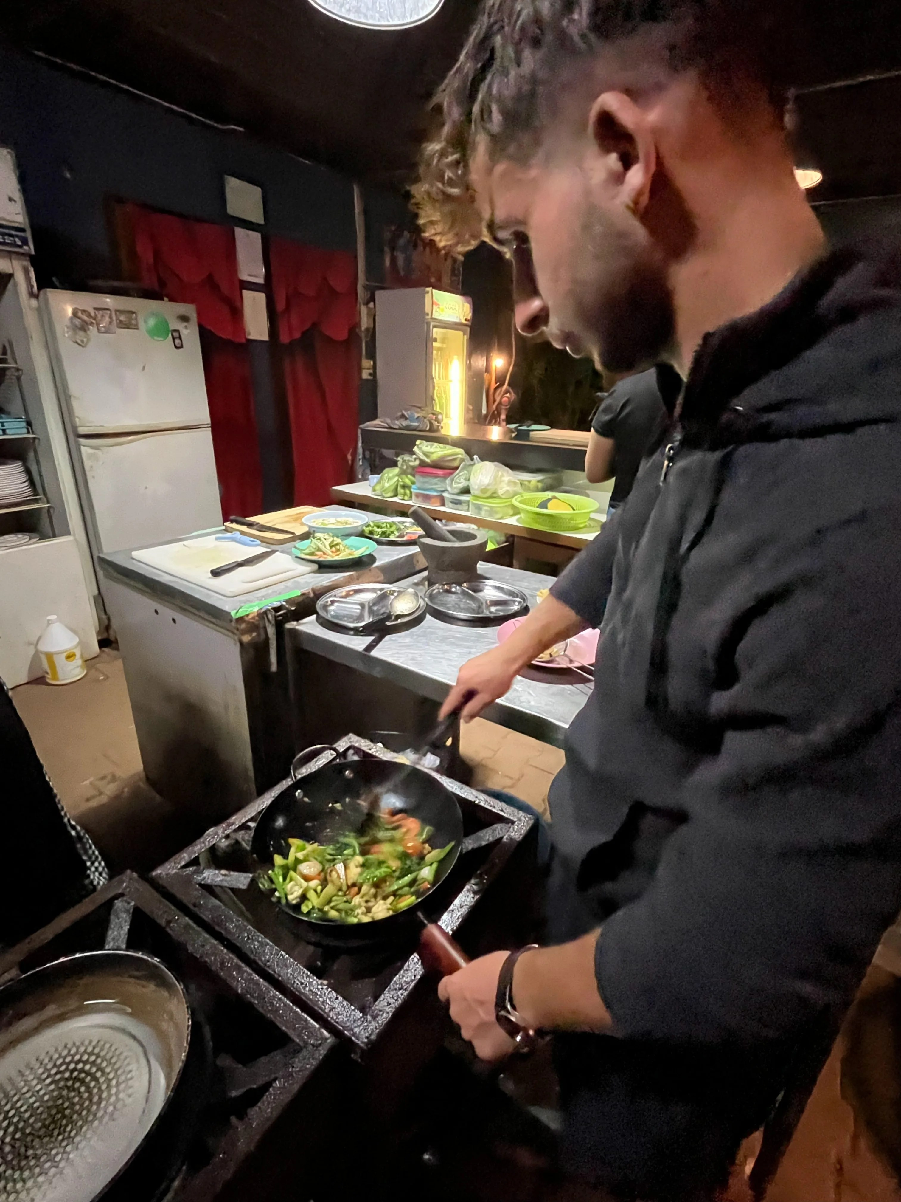 me cooking a stir fry in a wok during the nightly cook-your-own-dinner at crossroads house hostel in mae hong son