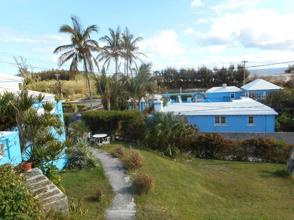 blue cottages and a garden path at blue horizons guest house in warwick, bermuda, with the ocean in the distance