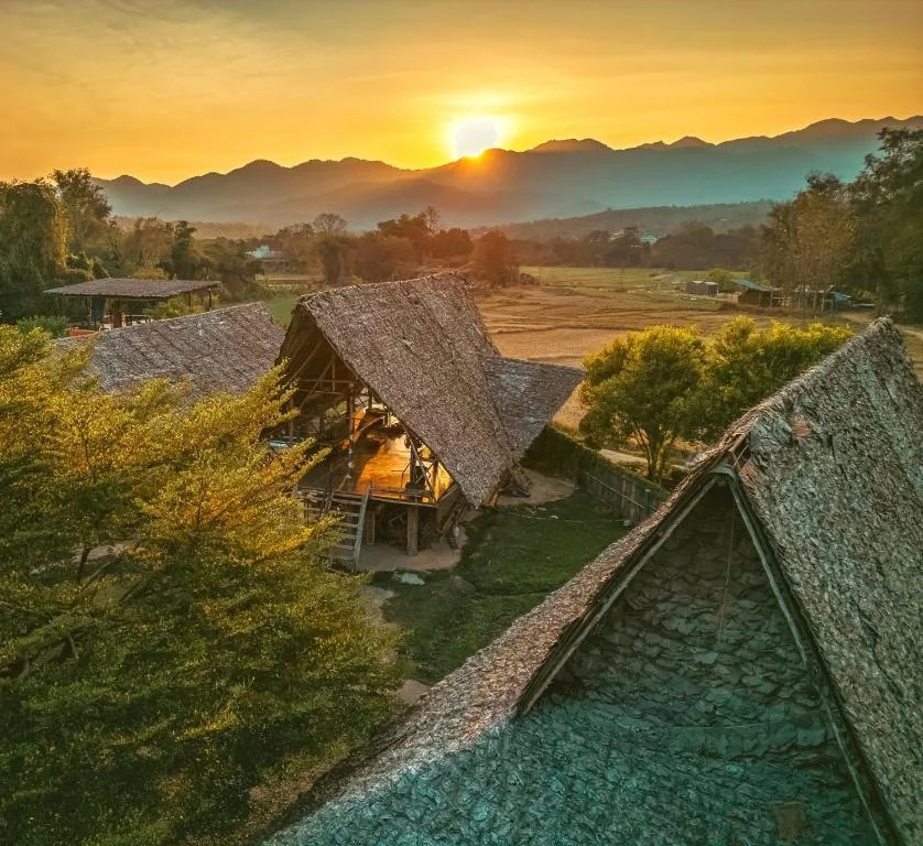 sunset over the mountains of pai seen from the thatched-roof buildings of cody backpackers hostel