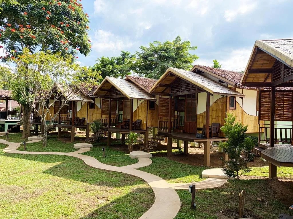 row of wooden bungalows on stilts along a winding garden path at pai country hut in pai, thailand