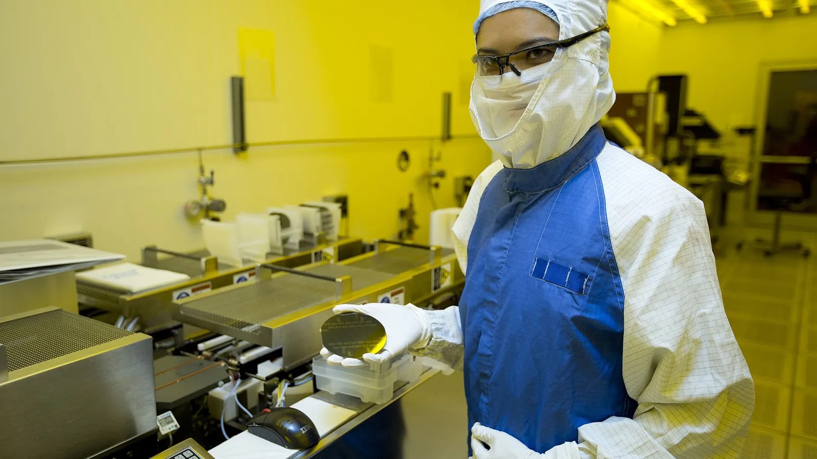 A researcher in a cleanroom suit holds up a finished silicon wafer