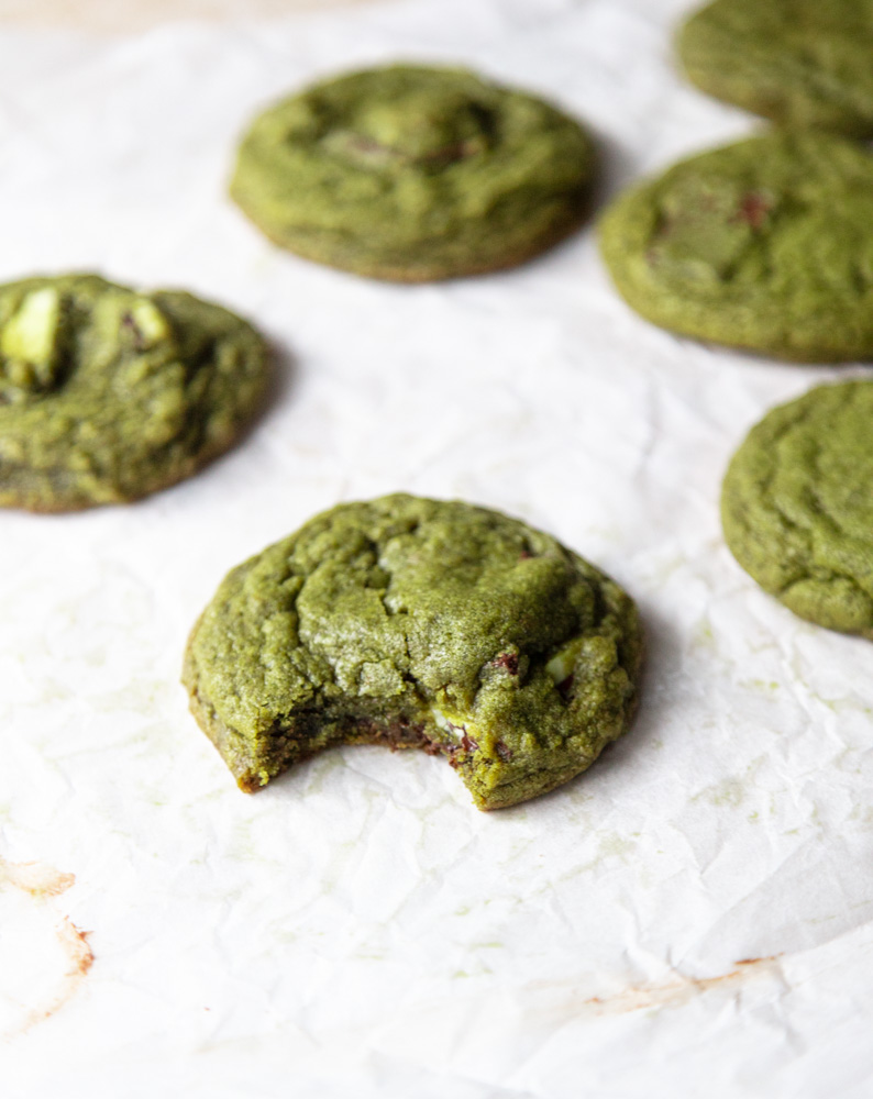 matcha cookies on parchment paper with one cookie bitten into