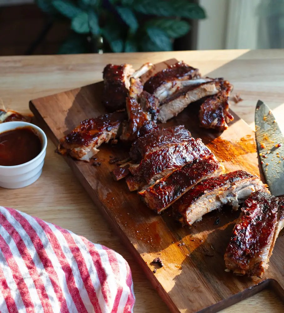 oven baked st louis style bbq ribs cut in pieces on a cutting board with a knife and bbq sauce on the side