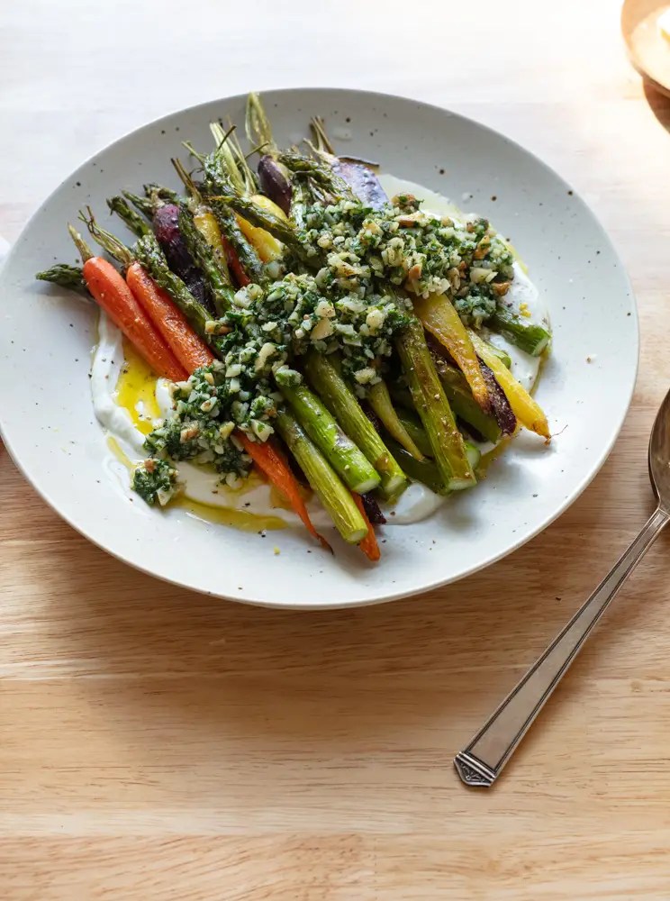 Roasted asparagus and carrots on a bed of yogurt with chunky pesto on top.