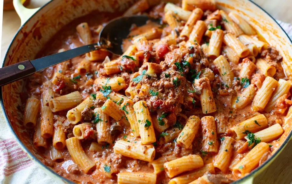 close up of rigatoni in creamy bolognese sauce in a yellow large skillet