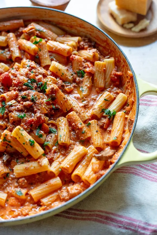 skillet filled with rigatoni and meat sauce with parmesan cheese on a small plate above